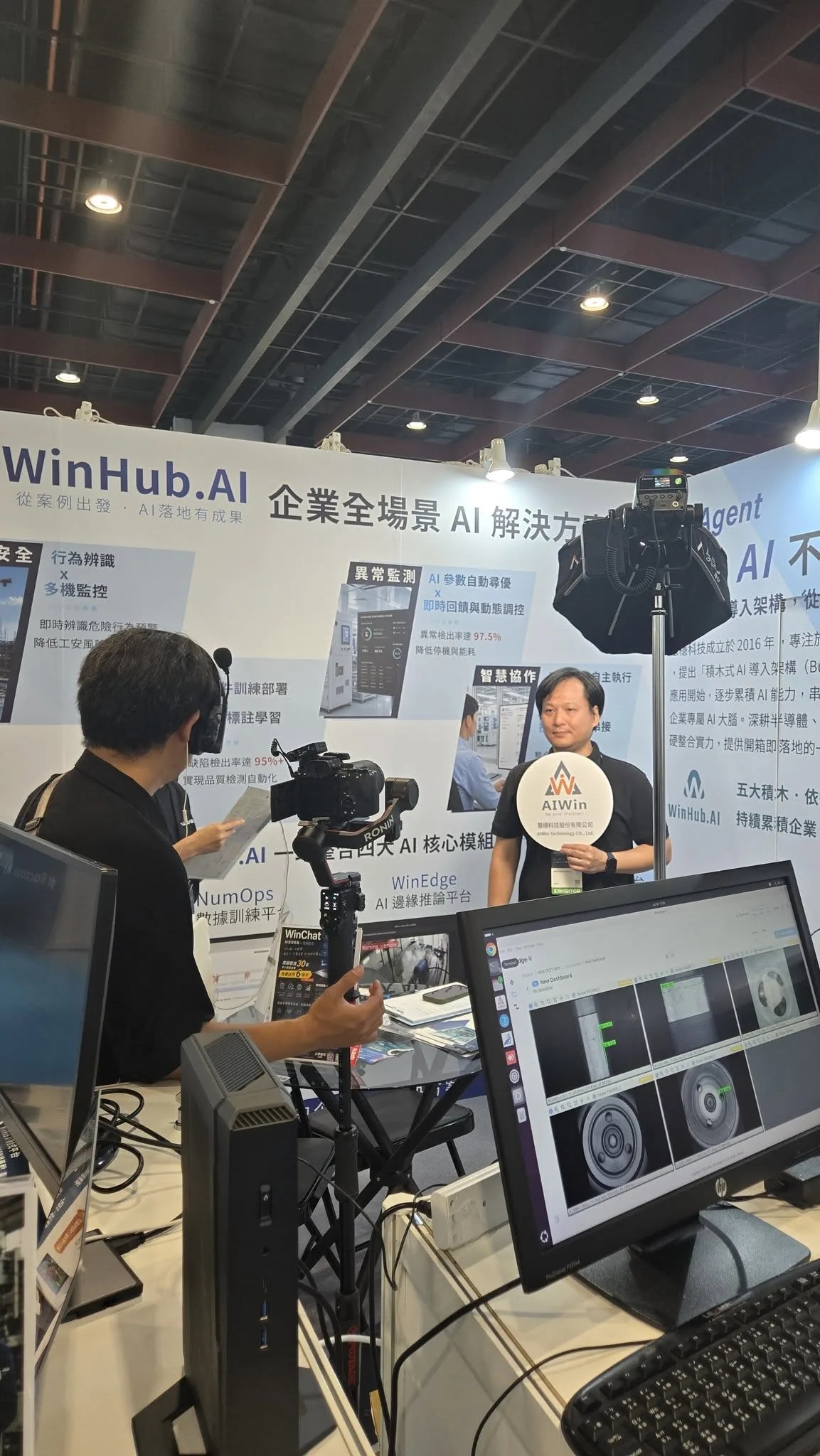 媒體在慧穩科技攤位採訪拍攝,前方螢幕顯示 AI 瑕疵檢測畫面